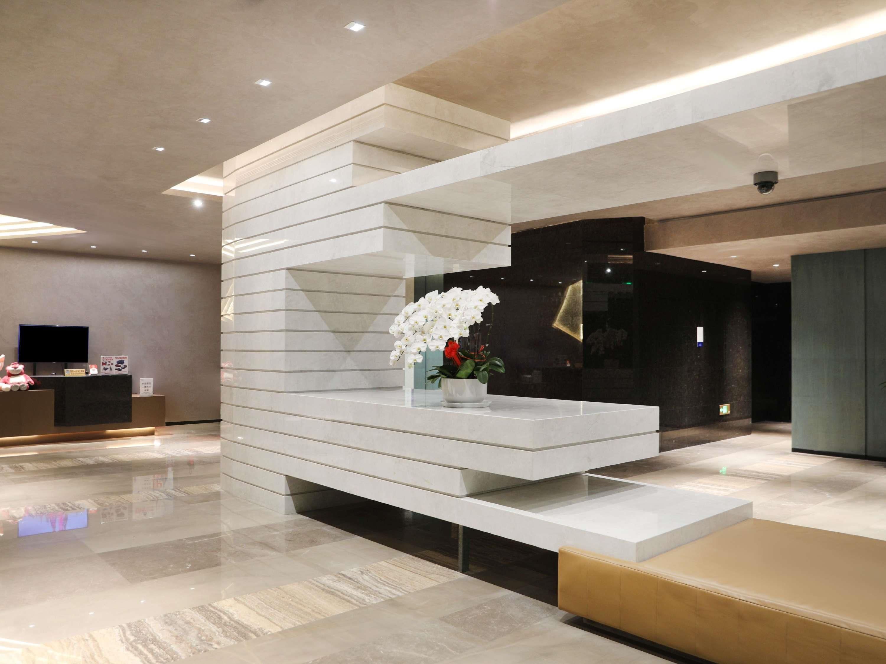 Una moderna zona de recepción con un mostrador escalonado, un televisor de pantalla plana y un jarrón con flores blancas.