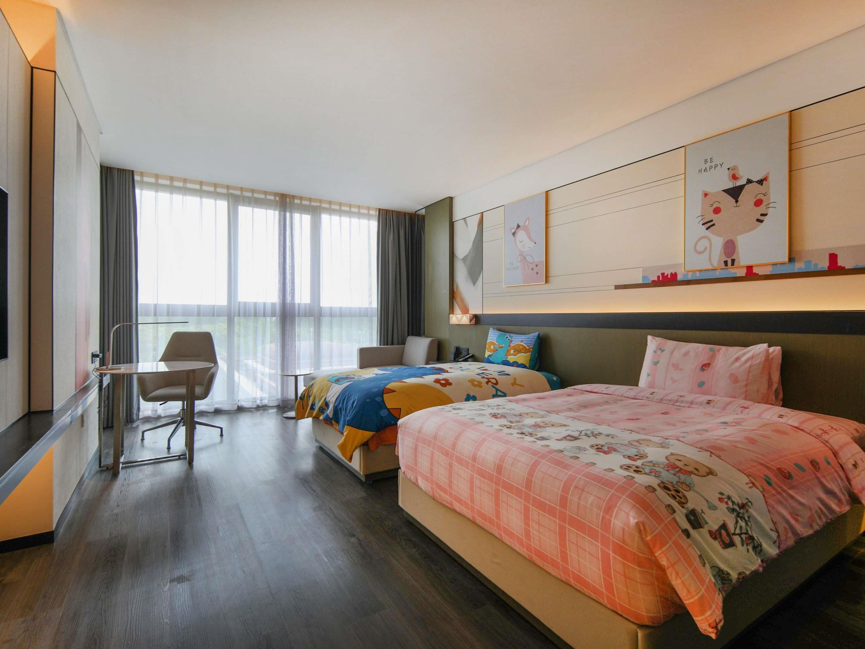 Une chambre d’hôtel avec deux lits, un bureau et une grande fenêtre avec des rideaux.