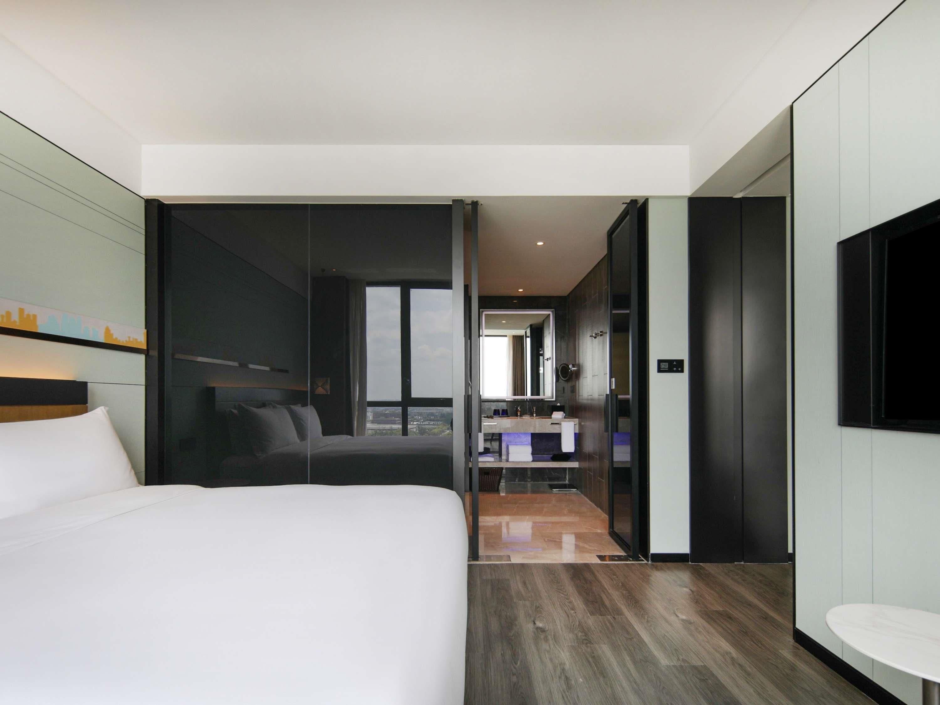A modern hotel room with a large bed, a bathroom with a vanity, and a city view.