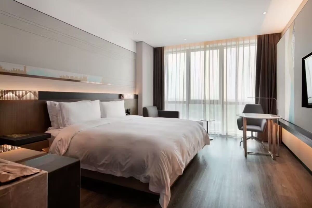 A modern hotel room with a large bed, a desk, a chair, and a TV.