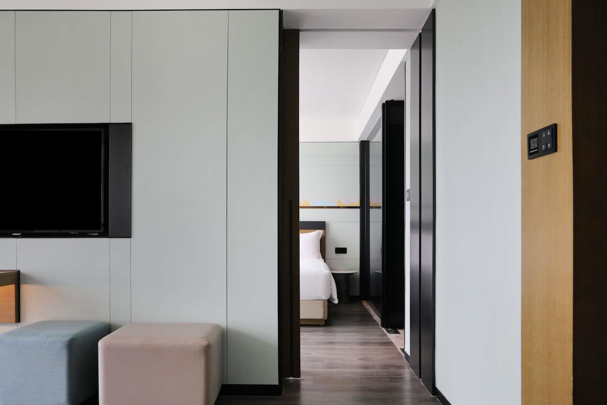 A modern hotel room with a flat-screen TV, a bed, a small table, and a bench.
