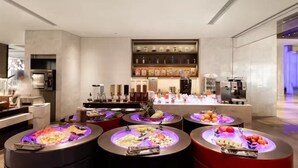 A modern hotel lobby with a self-service food station featuring various fruits and vegetables.