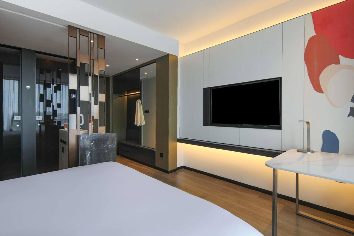 A modern hotel room with a large bed, a TV mounted on the wall, and a small table.