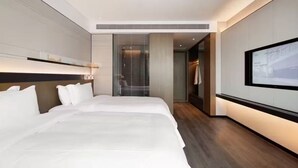 A modern hotel room with two beds, a large flat-screen TV, and a view of the cityscape through the window.
