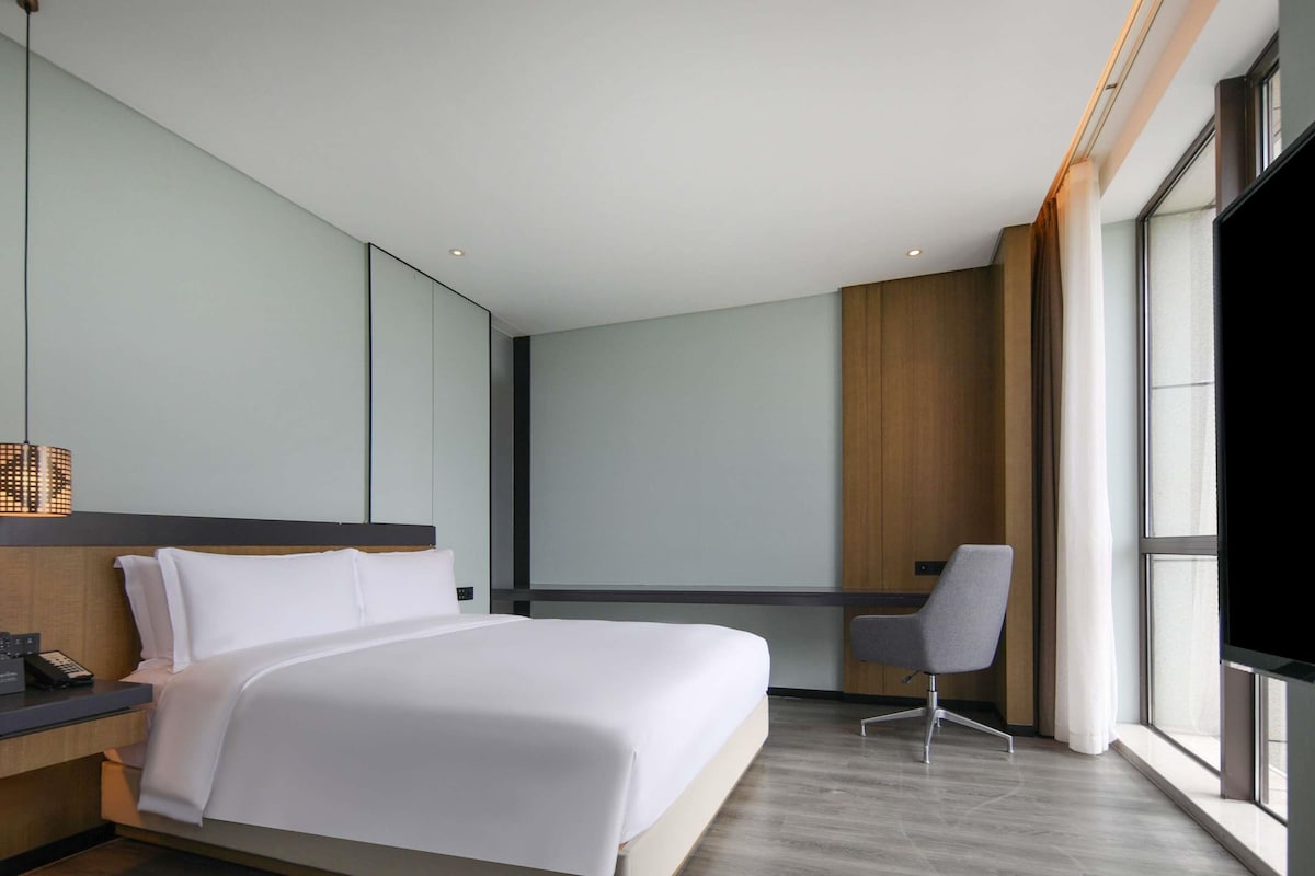 A modern hotel room with a large bed, a desk, and a chair.