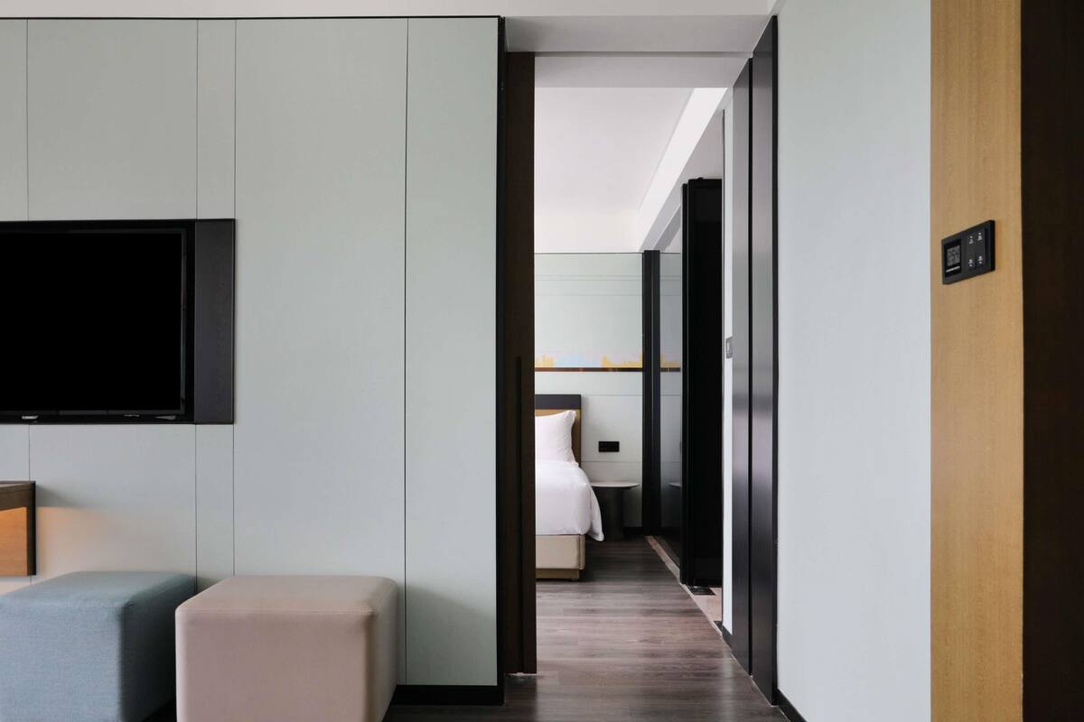 A modern hotel room with a flat-screen TV, a bed, a small table, and a bench.