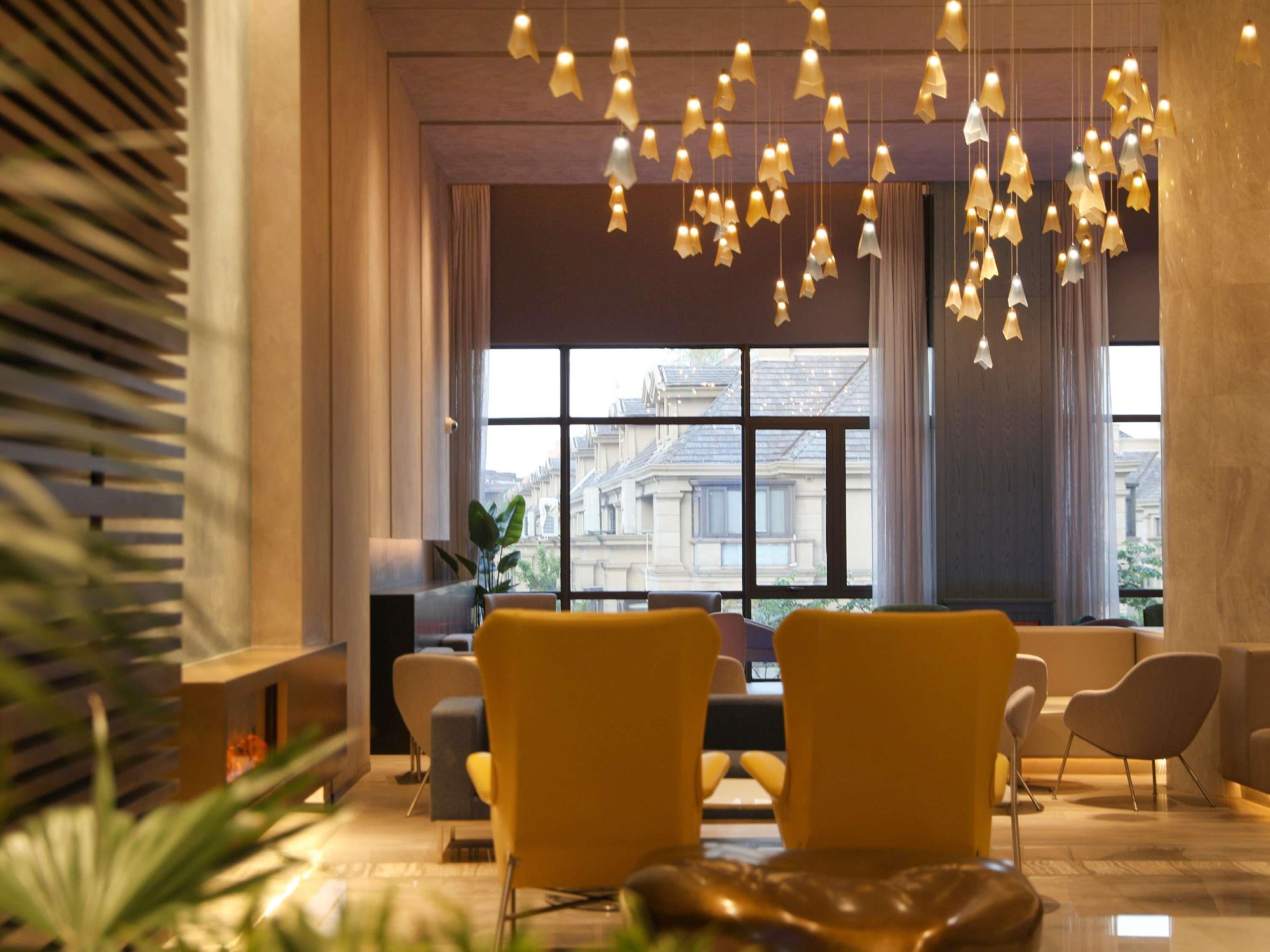 Un hall d’entrée moderne avec une grande fenêtre, deux fauteuils jaunes et un luminaire suspendu.