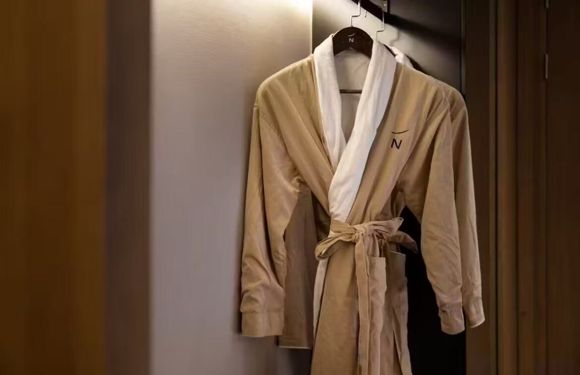 A beige robe hanging on a wooden hanger in a room with a wooden door and a white wall.