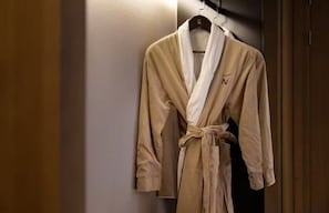 A beige robe hanging on a wooden hanger in a room with a wooden door and a white wall. - Novotel Shanghai Chuansha (Shanghai)