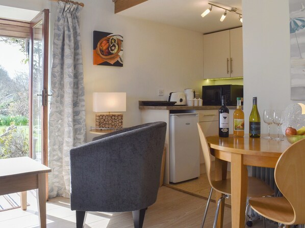 A compact kitchen with a dining area, a refrigerator, a microwave, a coffee maker, and a wine bottle on the counter.