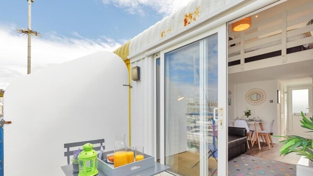 A balcony with a table set for breakfast, a sliding glass door leading to a dining area, and a view of the city.