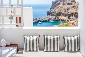 Una habitación con una cama, almohadas, una mesita y vistas a un paisaje costero con barcos.