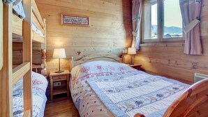 Ein gemütliches Blockhausszimmer mit Holzvertäfelung, einem Bett mit Quiltdecke, einem Nachttisch mit Lampe und einem Fenster mit Vorhängen.