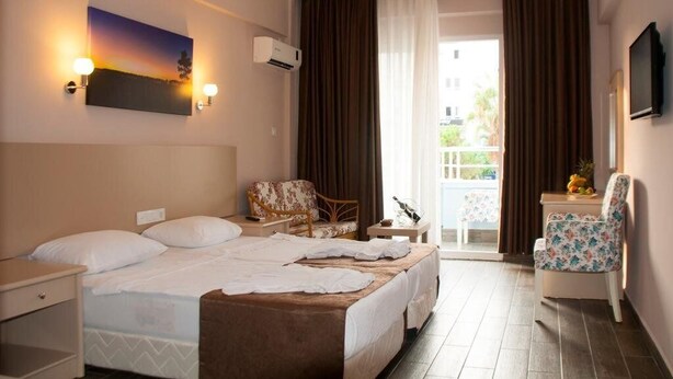 A hotel room with a bed, a chair, a small table, a painting, and a TV. - Suit Klas More Anex (Alanya)
