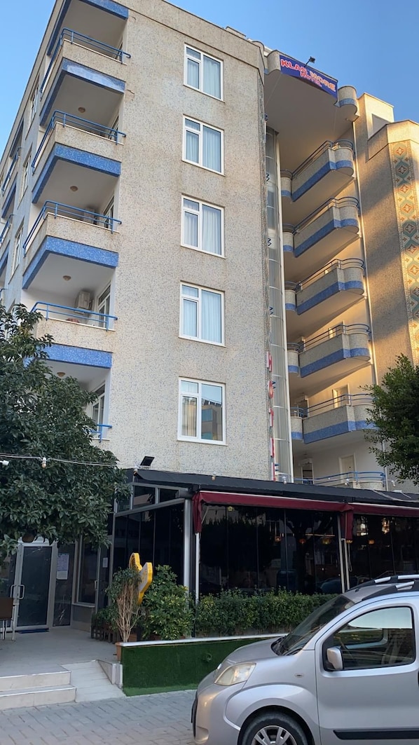A multi-story building with balconies, a visible restaurant entrance, and a car parked in front.
