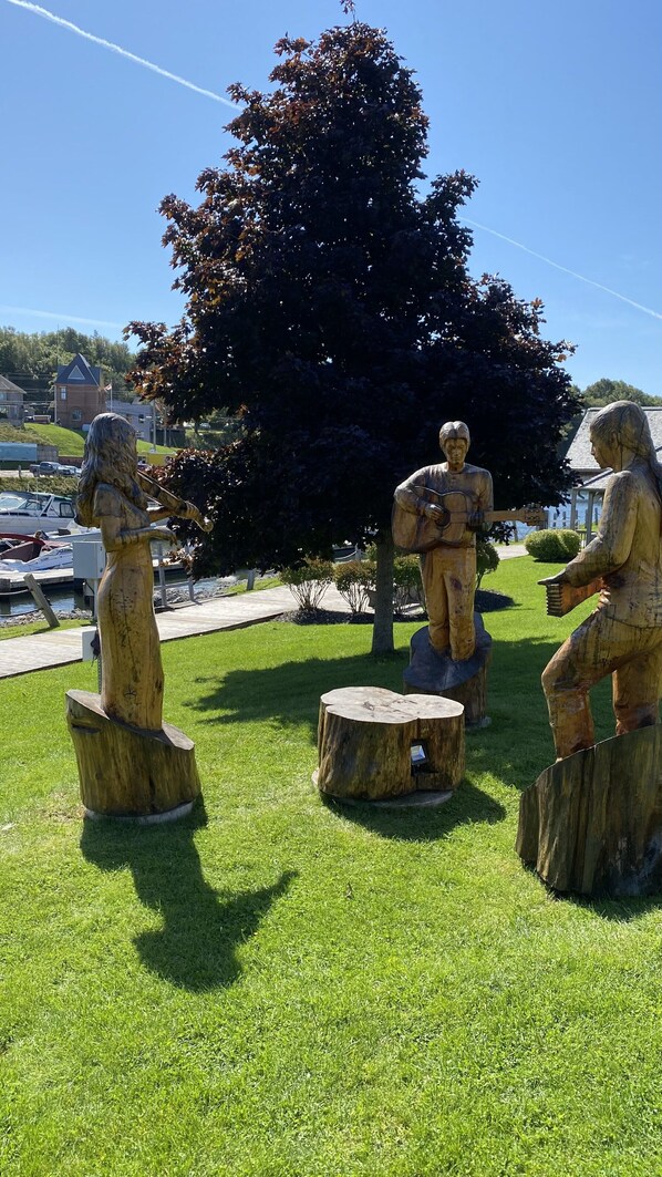 Esculturas de madera al aire libre de músicos sobre troncos de árboles en un parque.