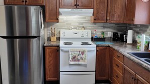 Une cuisine avec des meubles en bois, un réfrigérateur en acier inoxydable, une cuisinière blanche et un plan de travail en granit.
