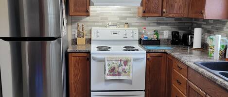 A kitchen with wooden cabinets, a stainless steel refrigerator, a white stove, and a granite countertop.