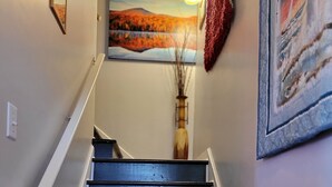 Un escalier aux marches sombres, avec des rampes blanches, et un tableau représentant un paysage accroché au mur au-dessus.
