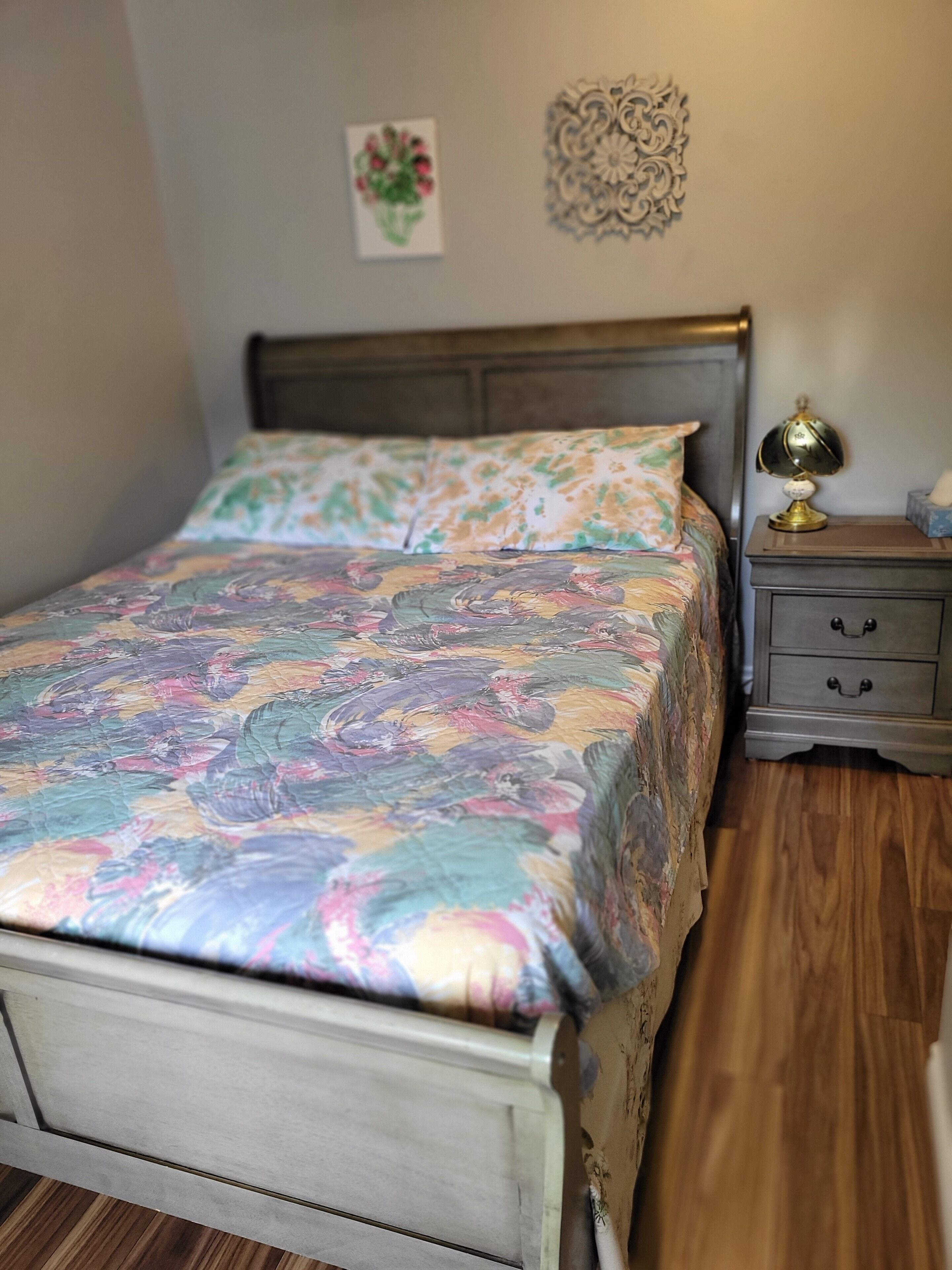 A bed with a floral bedspread, a nightstand with a lamp, and a wall decoration.