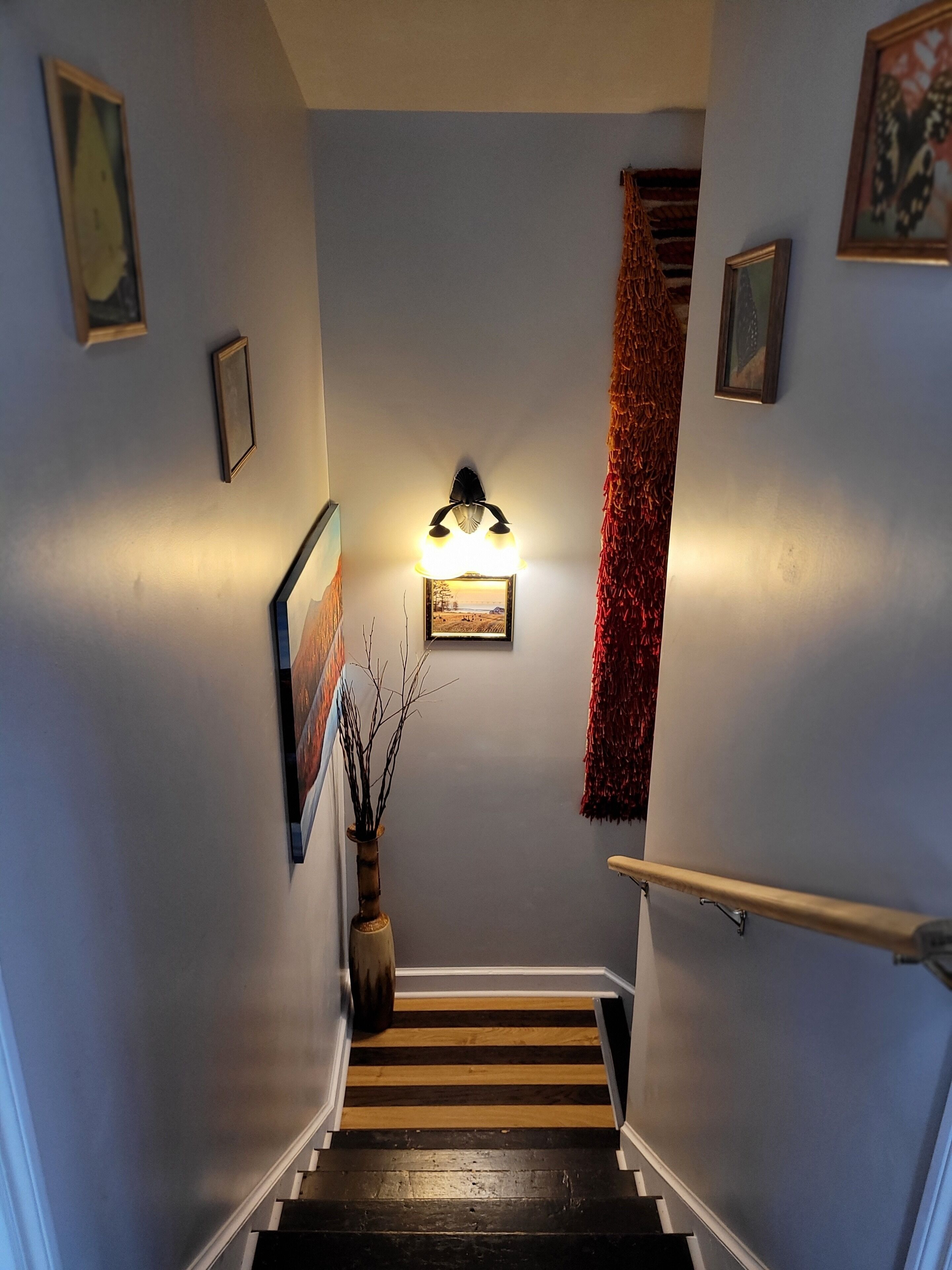 Un escalier avec une rampe en bois, un luminaire fixé au mur et des tableaux encadrés.