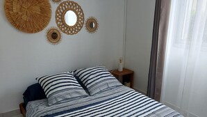 A bedroom with a bed, a nightstand, a wall-mounted air conditioner, and decorative wall art. - J&M'APART LOC SAISONNIERE SAINT GILLES LES BAINS (Saint Gilles Les Bains)