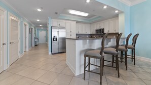 A modern kitchen with white cabinets, a central island with bar stools, and a stainless steel refrigerator. - Phoenix Orange Beach II 1404 by Liquid Life (Orange Beach)
