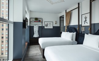 Een moderne hotelkamer met twee bedden, een zithoekje, een spiegel en uitzicht op de stad.