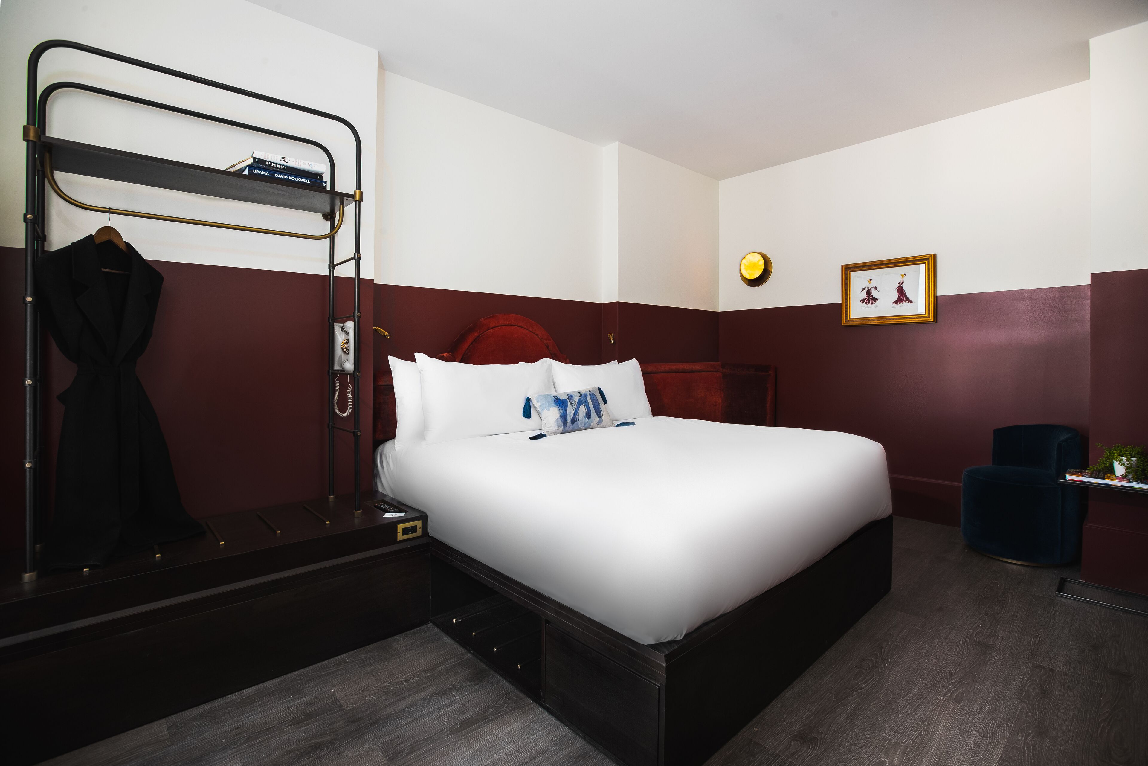 A hotel room with a bed, a bedside table, a wall-mounted shelf, a chair, and a picture on the wall.