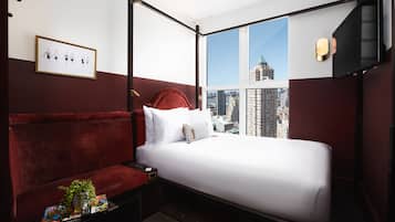 Habitación de hotel con cama con dosel, sofá rojo, vista a la ciudad y un cuadro en la pared.
