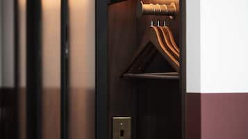 A wooden coat rack with a hanging coat and a door with a light switch.