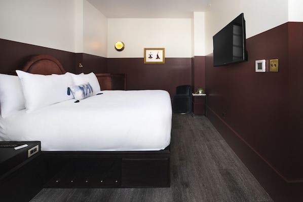 A hotel room with a large bed, a bedside table, a TV mounted on the wall, and a small table with a plant. - CIVILIAN Hotel (New York)