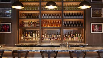 A bar with a checkered floor, wooden bar stools, and shelves of bottles.