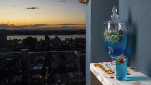 A city view at sunset, a glass container with a blue liquid, and a table with a glass and dried orange slices.