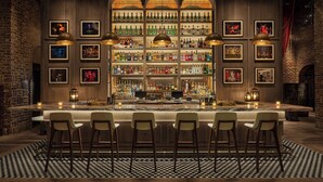 A bar with multiple shelves of liquor bottles, framed pictures on the walls, and bar stools.