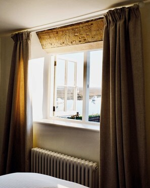 Ein Zimmer mit einem großen Fenster, einem Heizkörper darunter und Blick auf Strand und Boote.