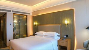 Ein Hotelzimmer mit einem großen Bett, einem hölzernen Kopfteil, zwei Nachttischlampen, einem Nachttisch und einer Duschkabine aus Glas.