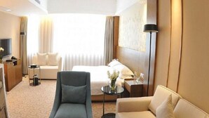 Ein Hotelzimmer mit einem Bett, zwei Sofas, einem Fernseher, einer Lampe und einem kleinen Tisch mit einer Vase.