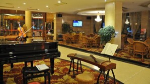 Eine Hotelhalle mit einem Flügel, bequemen Sitzgelegenheiten, einem Fernseher und einer großen Pflanze.