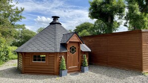 A small wooden cabin with a hexagonal roof, a door with a circular window, and two potted plants. - Beautiful Large Country Barn Conversion Hot Tub, Pool, BBQ Hut, Large Grounds (Lampeter)