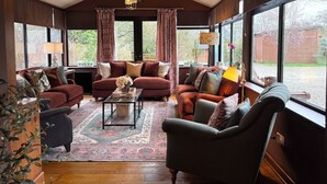 A cozy living room with a fireplace, large windows, and a chandelier. - Beautiful Large Country Barn Conversion Hot Tub, Pool, BBQ Hut, Large Grounds (Lampeter)