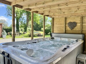 A hot tub with multiple jets, surrounded by a wooden deck and a heart-shaped wall decoration. - Beautiful Large Country Barn Conversion Hot Tub, Pool, BBQ Hut, Large Grounds (Lampeter)