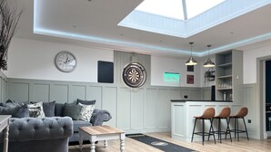 A modern living room with a grey sofa, a wooden coffee table, and a dartboard on the wall. - Beautiful Large Country Barn Conversion Hot Tub, Pool, BBQ Hut, Large Grounds (Lampeter)