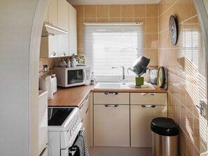 Una cocina compacta con microondas, tostadora, pileta y un pequeño basurero.