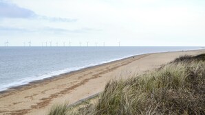 Een strand met een helder uitzicht op de oceaan en windturbines in de verte.