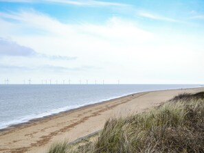Ein Strand mit freiem Blick auf das Meer und Windkraftanlagen in der Ferne.