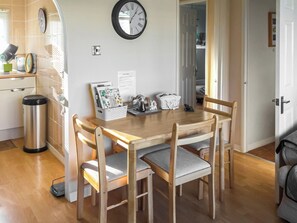 A dining area with a wooden table, four chairs, a wall clock, and a trash bin.