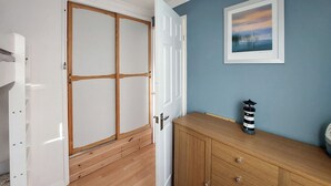 Een kamer met een houten garderobe, een dressoir met lades, een lijst met een foto aan de muur, en een lamp op het dressoir.