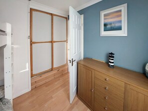 Ein Zimmer mit einem Holzschrank, einer Kommode und einem gerahmten Bild an der Wand. Eine Lampe steht auf der Kommode.