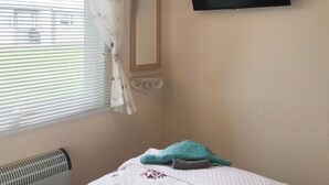 Een kamer met een bed, een aan de muur bevestigde televisie en een raam met zonwering.